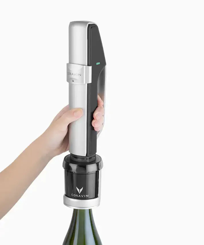 A hand holding a Coravin Sparkling Wine Preservation System with a bottle and black and silver device.