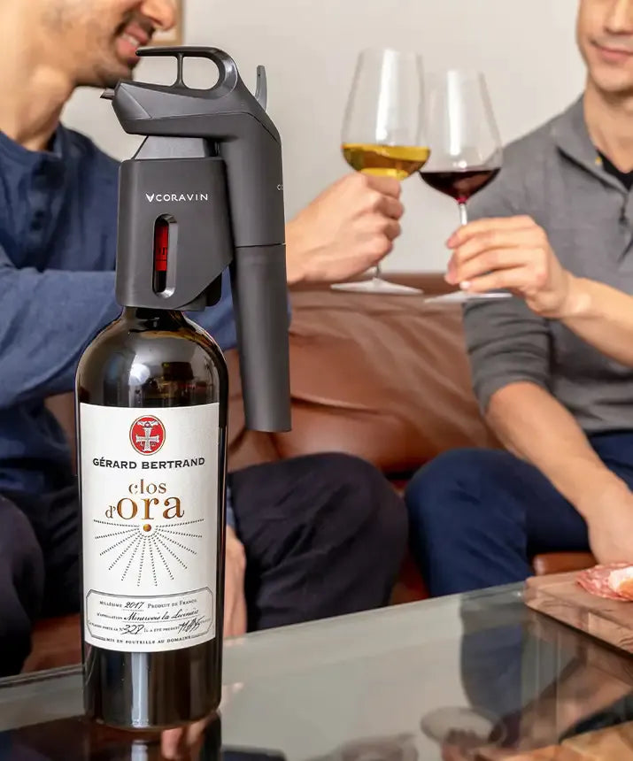 Coravin Timeless Three+ Wine Preservation System: A wine bottle with a gun on a table, people sitting on a couch, a person holding a glass of wine, and a close-up of a glass of wine.