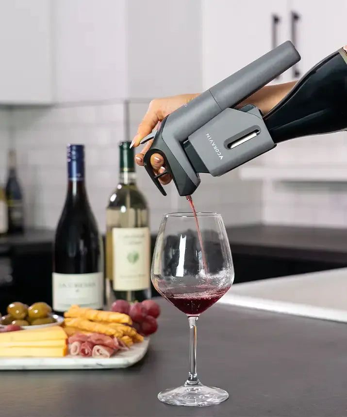 A person pouring wine into a glass using the Coravin Timeless Three SL Wine Preservation System.