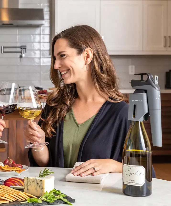 A woman holding wine glasses and a glass of wine, showcasing the Coravin Timeless Three SL Wine Preservation System.