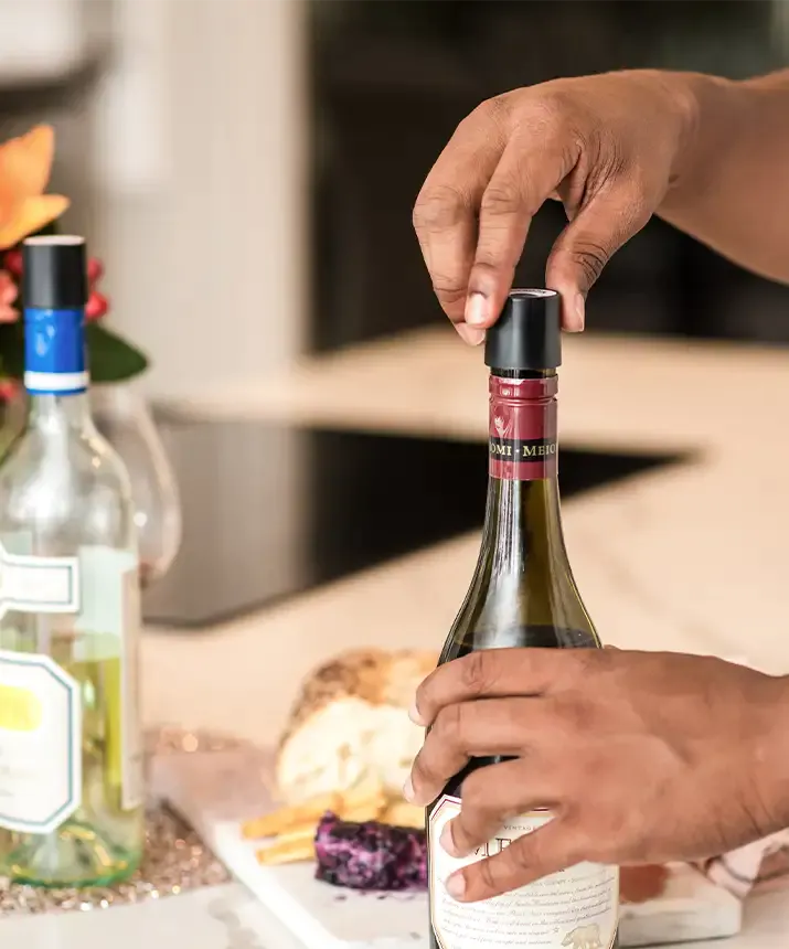 A person opening a bottle of wine with Coravin Screw Caps, compatible with most screw cap bottles.