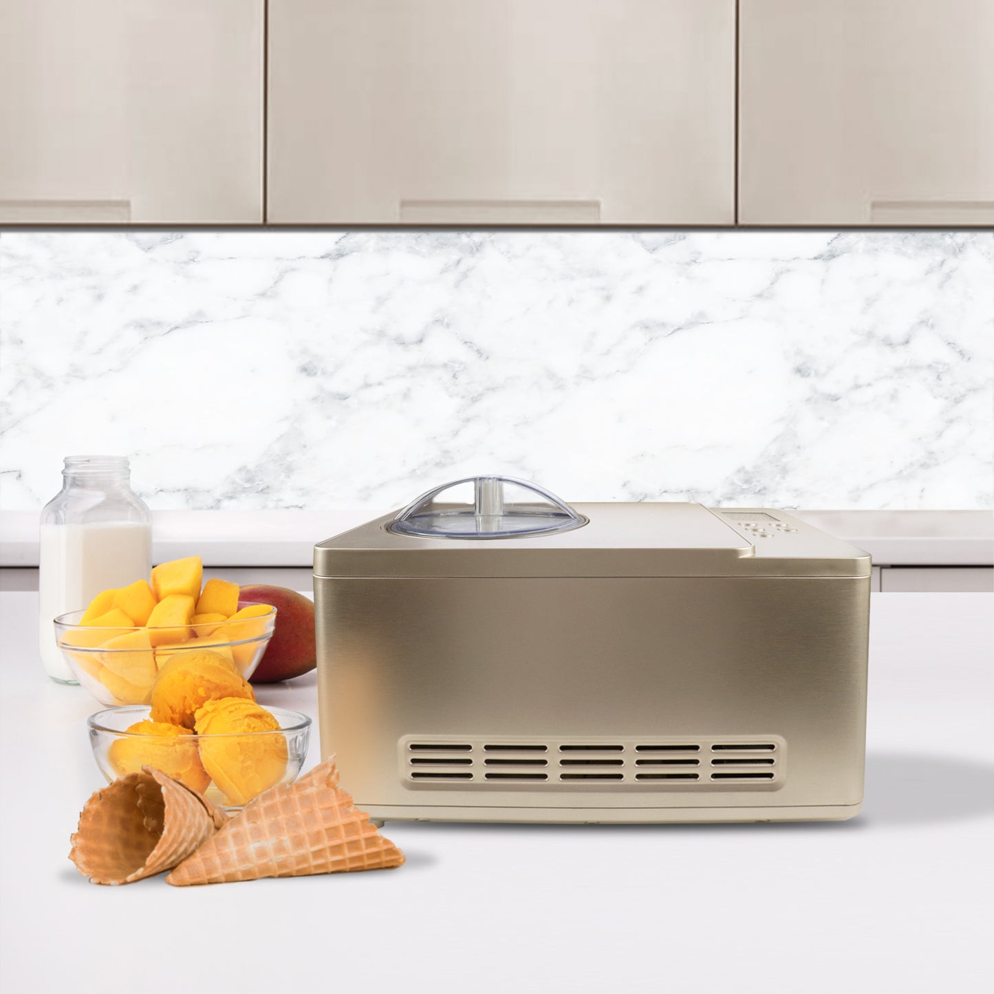 A machine with ice cream cones and fruit on a counter, including a silver rectangular object with a clear lid and a glass bottle of milk and a bowl of mangoes.